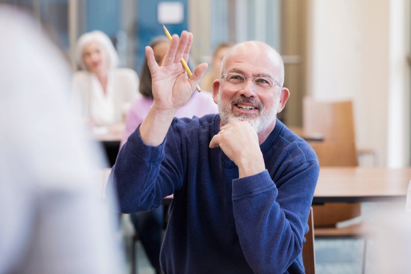 Senior man raising his hand to ask a question at an educational event.