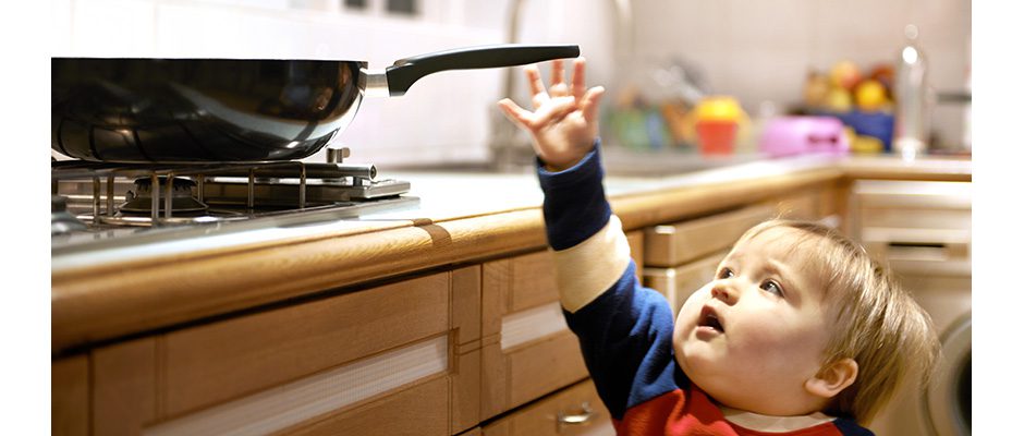 Young boy reaching for a hot pan on a hob