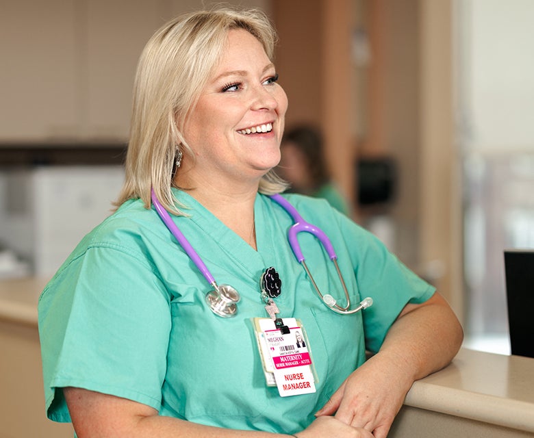 Close-up of a blonde nurse manager in scrubs, smiling to someone off-camera while demonstrating active listening.
