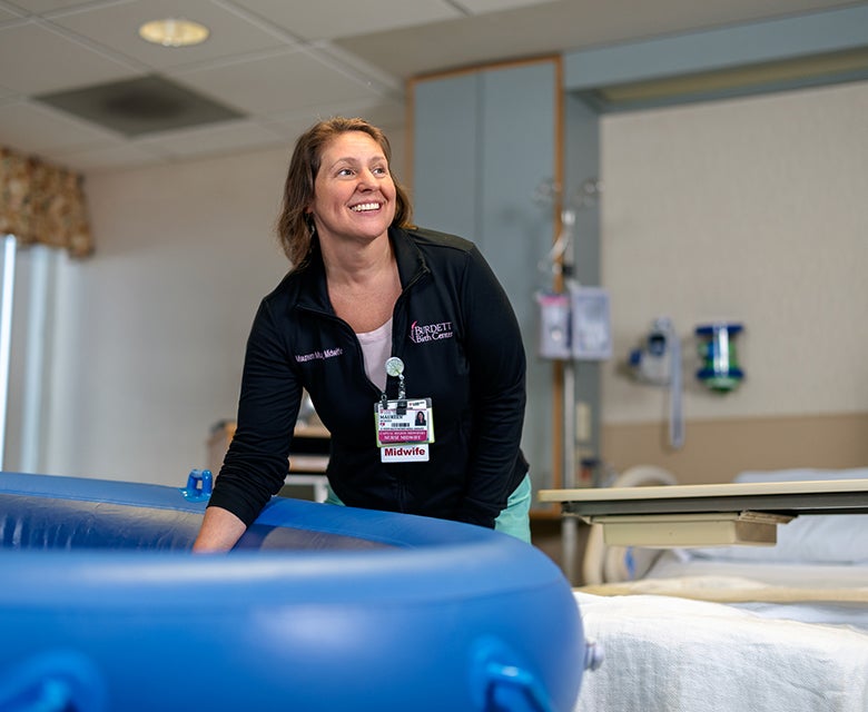 A female midwife with years of experience in Troy smiles and prepares the water-birth birthing pool for a maternity patient.