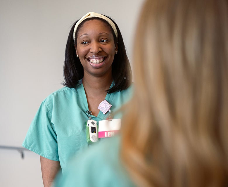 Closeup of a young female labor and delivery LPN smiling during a morning huddle in the hospital hallway.