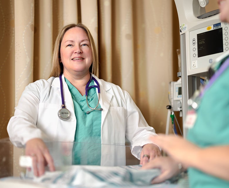 An experienced female pediatric NP in a white lab coat stands over a monitoring bassinet in the on-site, high-tech nursery.