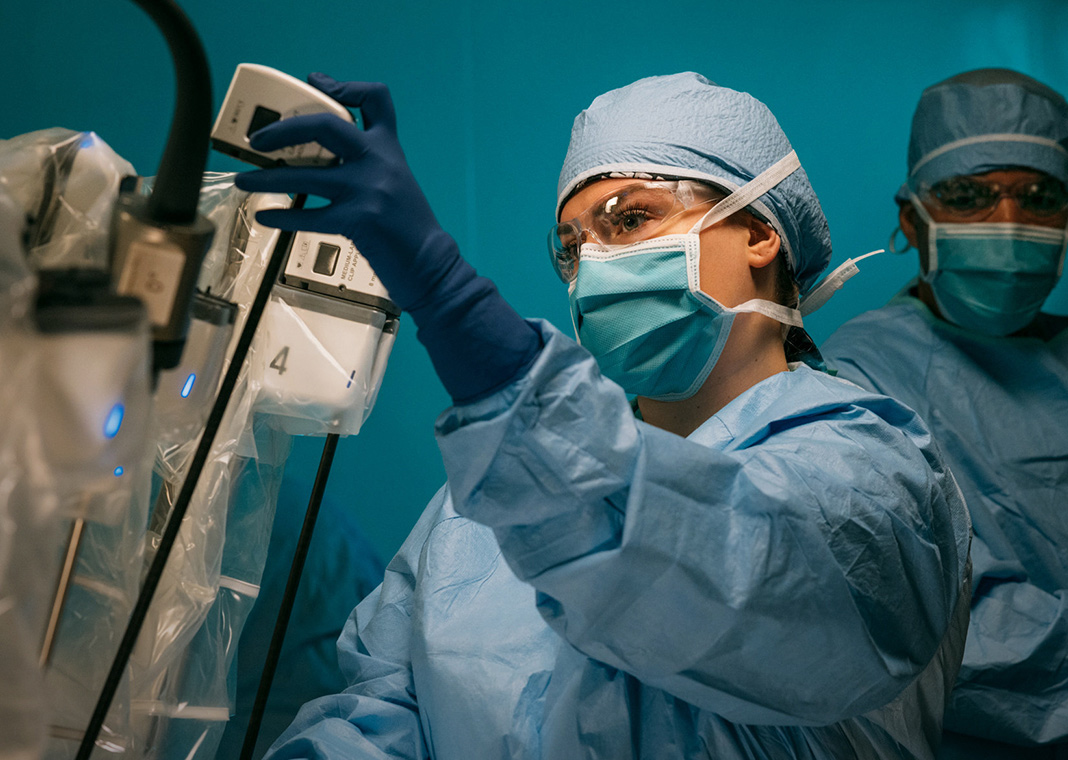 A technician in full PPE at St. Peter's Health Partners makes an adjustment to a Da Vinci machine ahead of surgery.